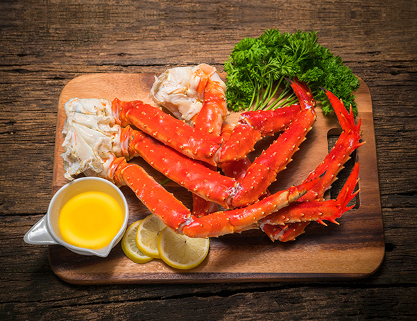 Photo of Alaska King Crab Legs surrounded by garnish and a cup of butter, atop a wooden tray.