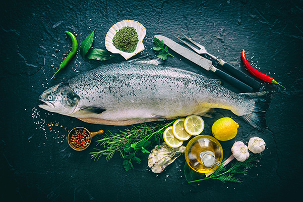 Photo of Salmon surrounded by cooking ingredients atop a dark background.