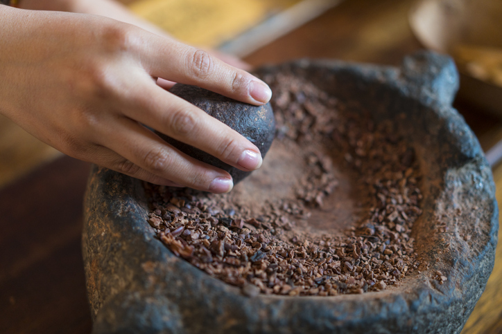 A woman’s hand with a stone grinder grinds cocoa and prepares cacao for a chocolate drink.
