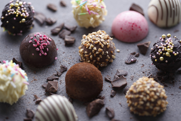 Various Chocolate Pralines and chocolate pieces on grey surface